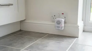 A compact plug in mouse repeller installed near floor level in a fitted kitchen